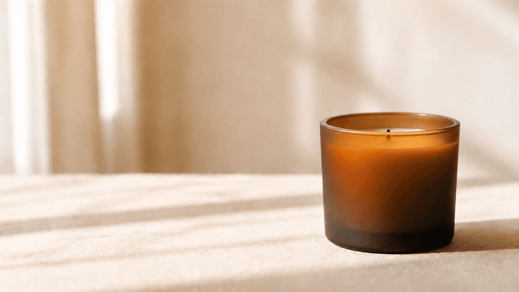 A lit beeswax candle in Bee Lighted's amber glass vessel in soft morning light