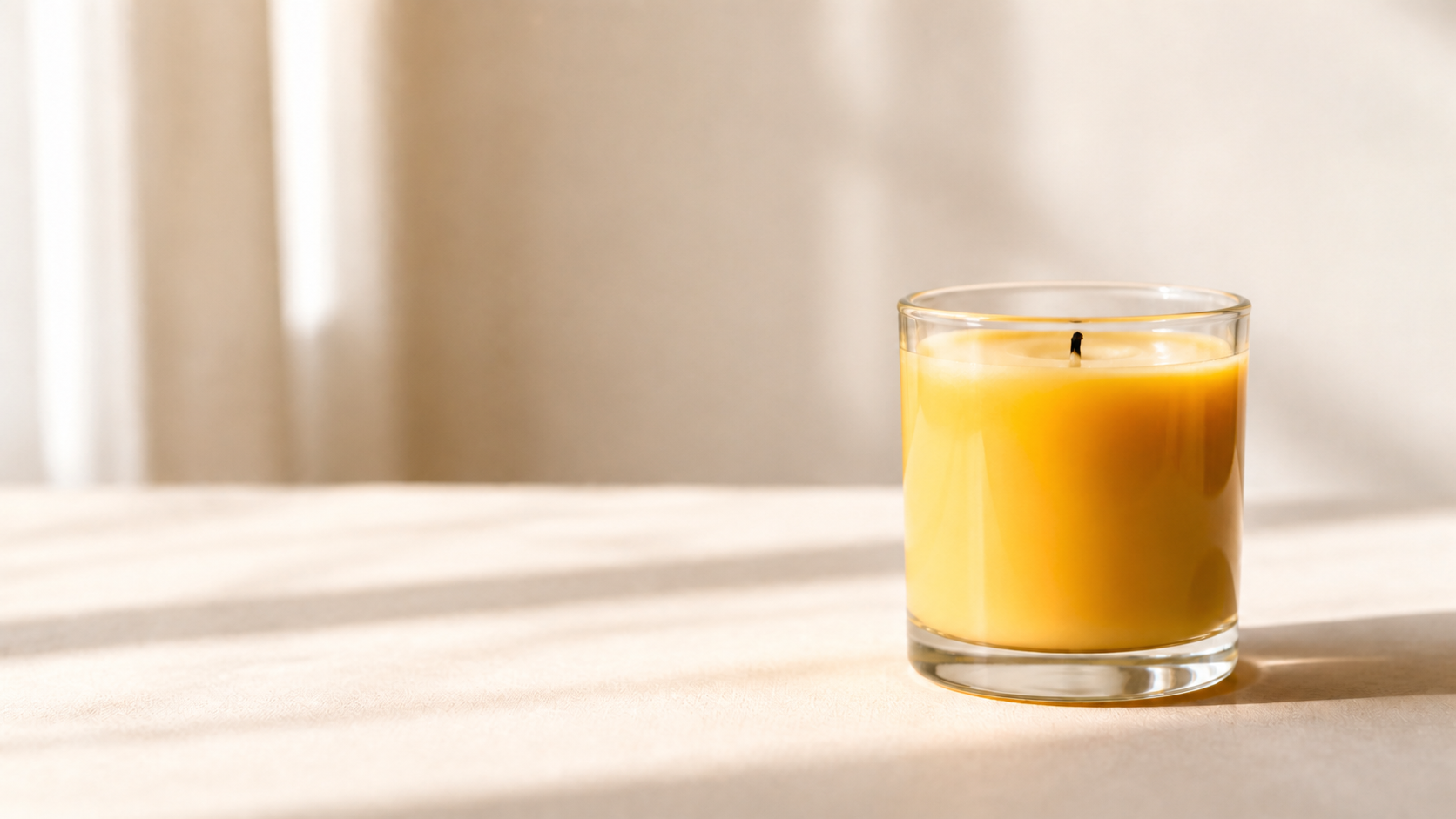 A lit golden beeswax candle in a clear glass jar in soft morning light